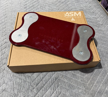 A dark red and silver ASM fitness plate resting on its brown cardboard box, placed on a gray quilted blanket.